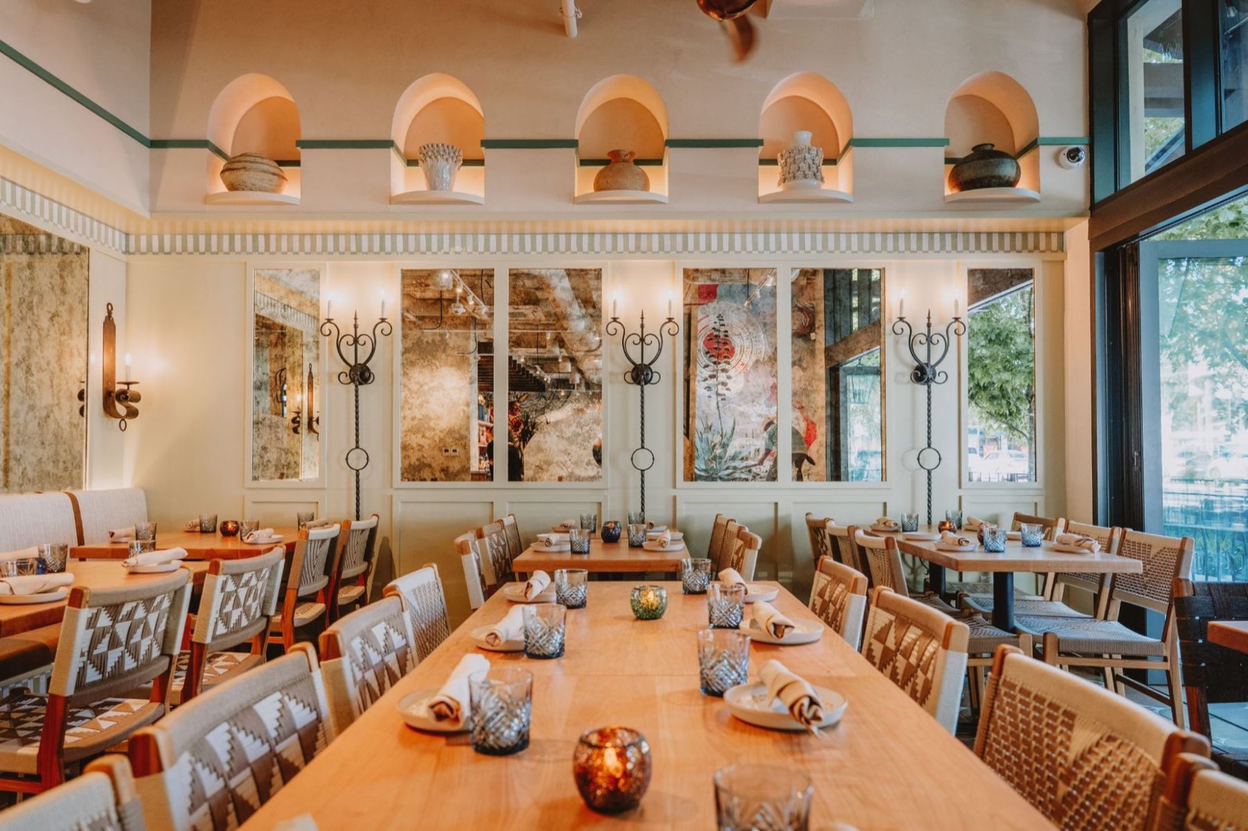 Alisios — long communal table set beneath arched display niches, wrought-iron candle sconces and tall windows